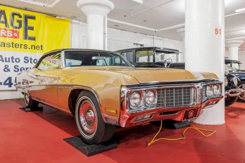 Vintage gold and chrome classic car parked indoors on red floor with other collector vehicles