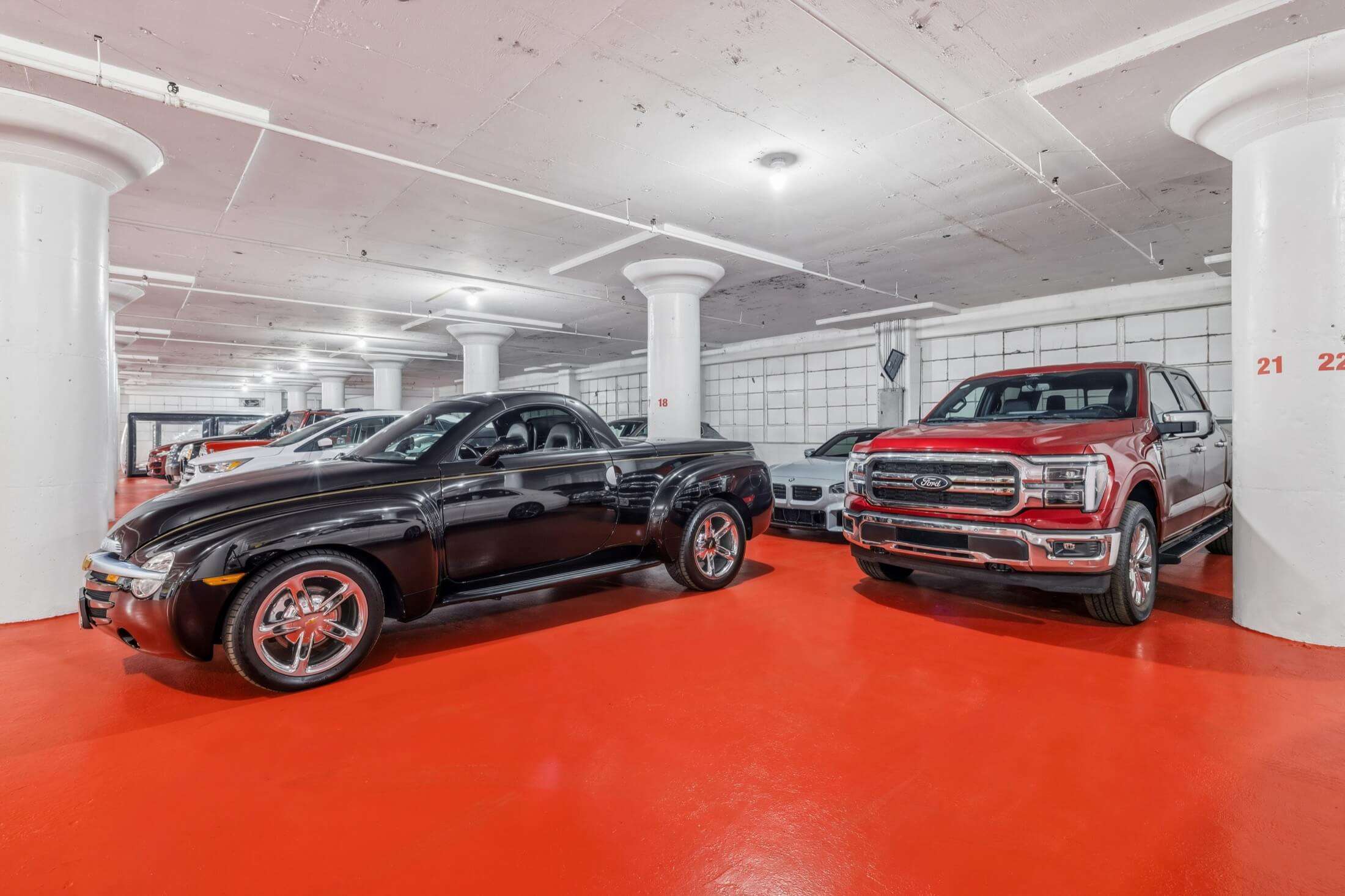 Indoor storage with black sports car, white coupe, and red pickup truck on bright red polished floor