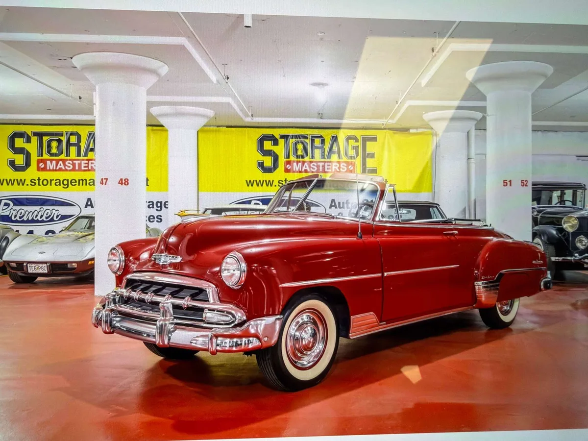 Vintage red convertible with whitewall tires parked inside our storage facility among classic cars