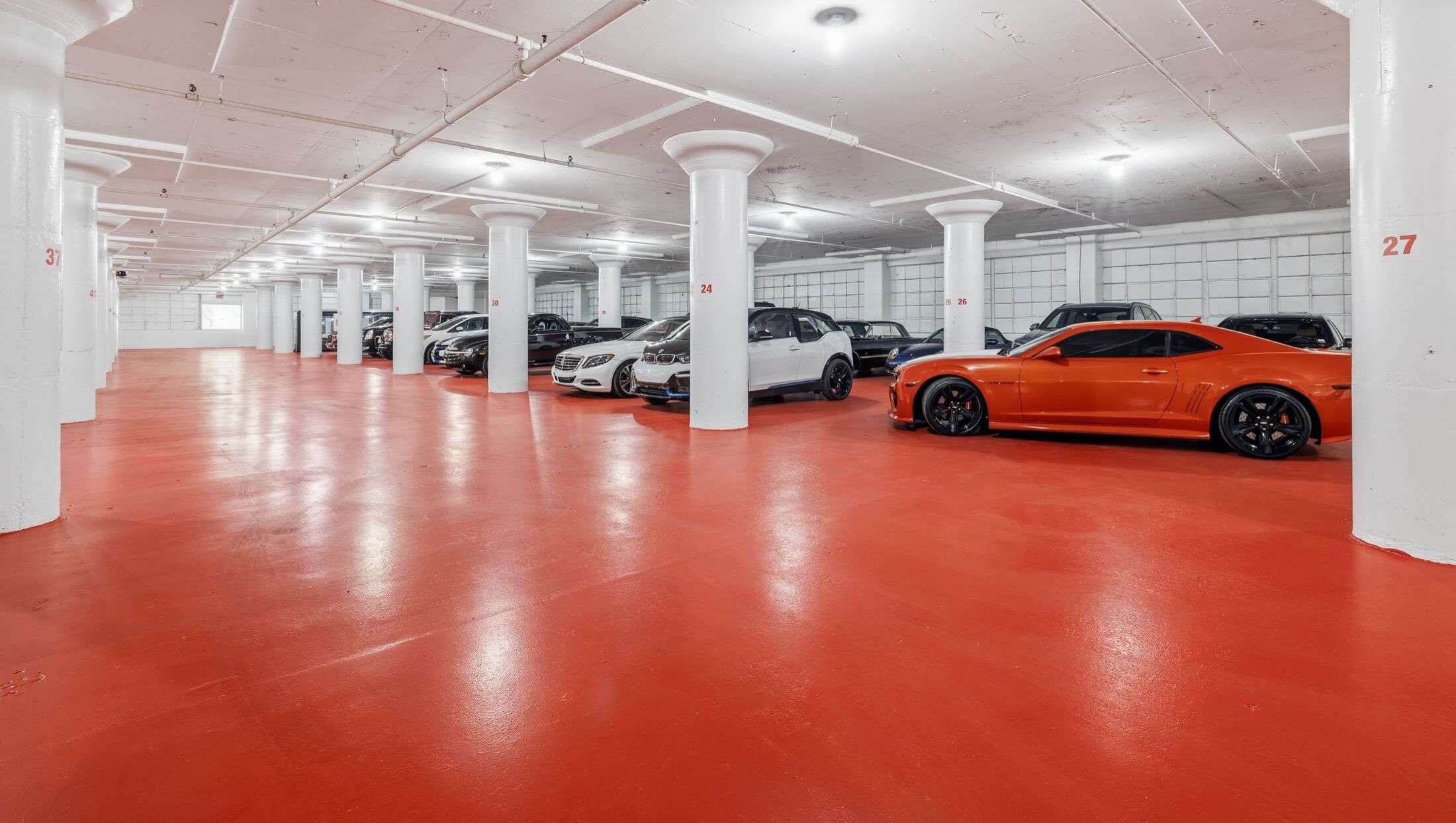 Indoor vehicle storage with luxury cars, white support columns and polished red concrete floor